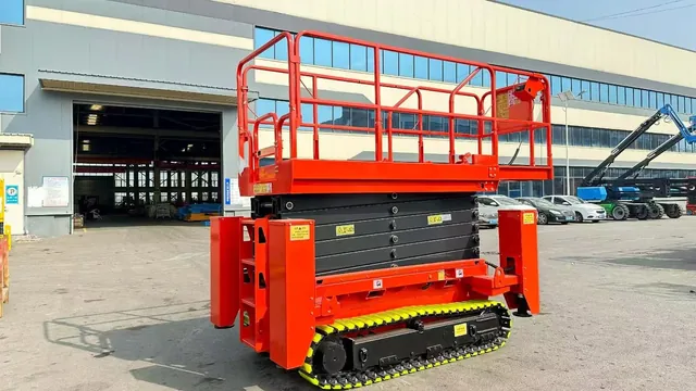 Red crawler scissor lift with stabilizer legs outside an industrial building